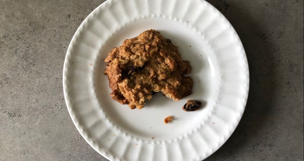Oatmeal raisin cookie with bite taken and crumbs, on plate