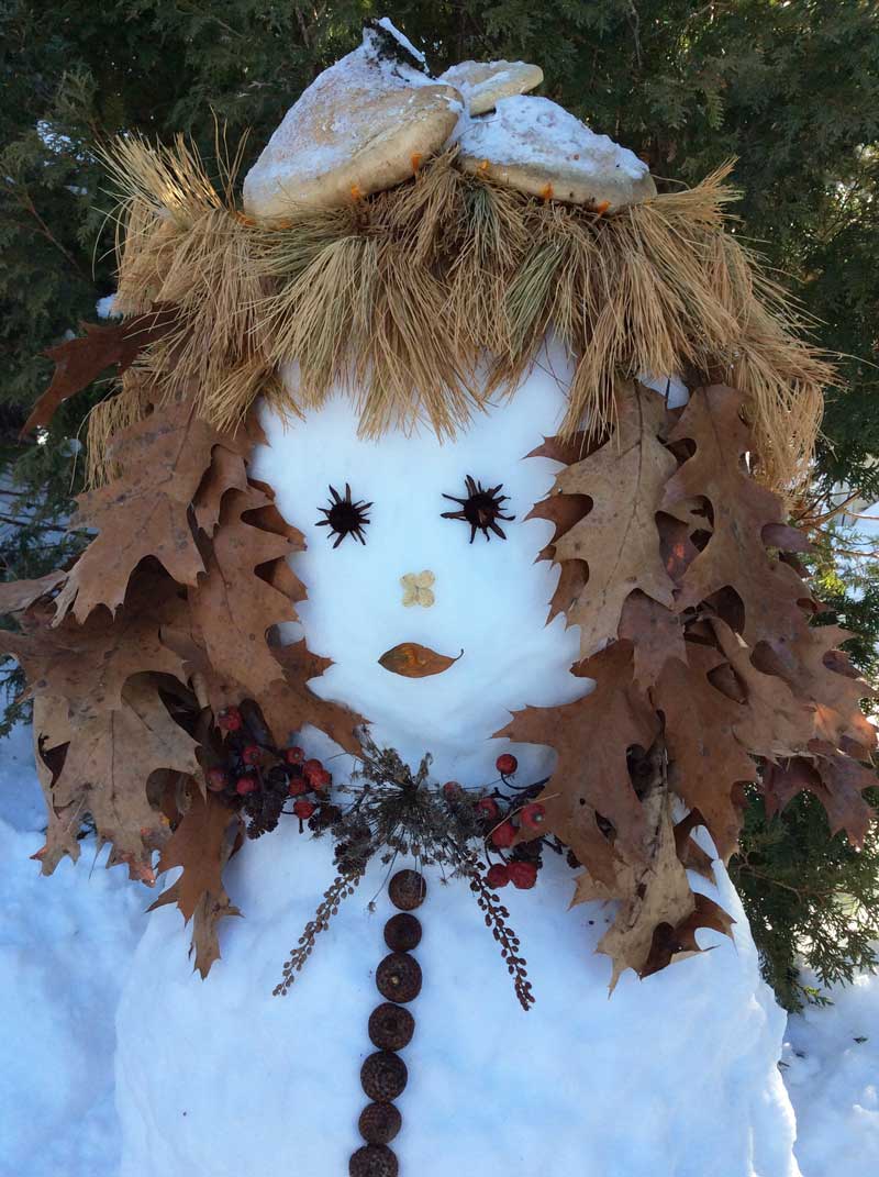image of a winter beauty made from snow with a mushroom cap, oak leaves for hair, and natural elements for the eyes, nose, mouth and necklace