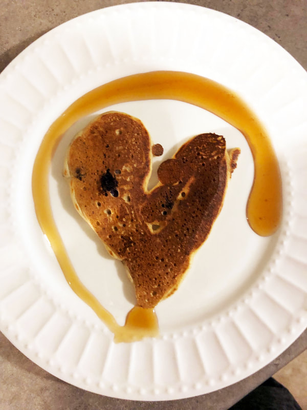 heart shaped pancake with a swirl of syrup on a white plate