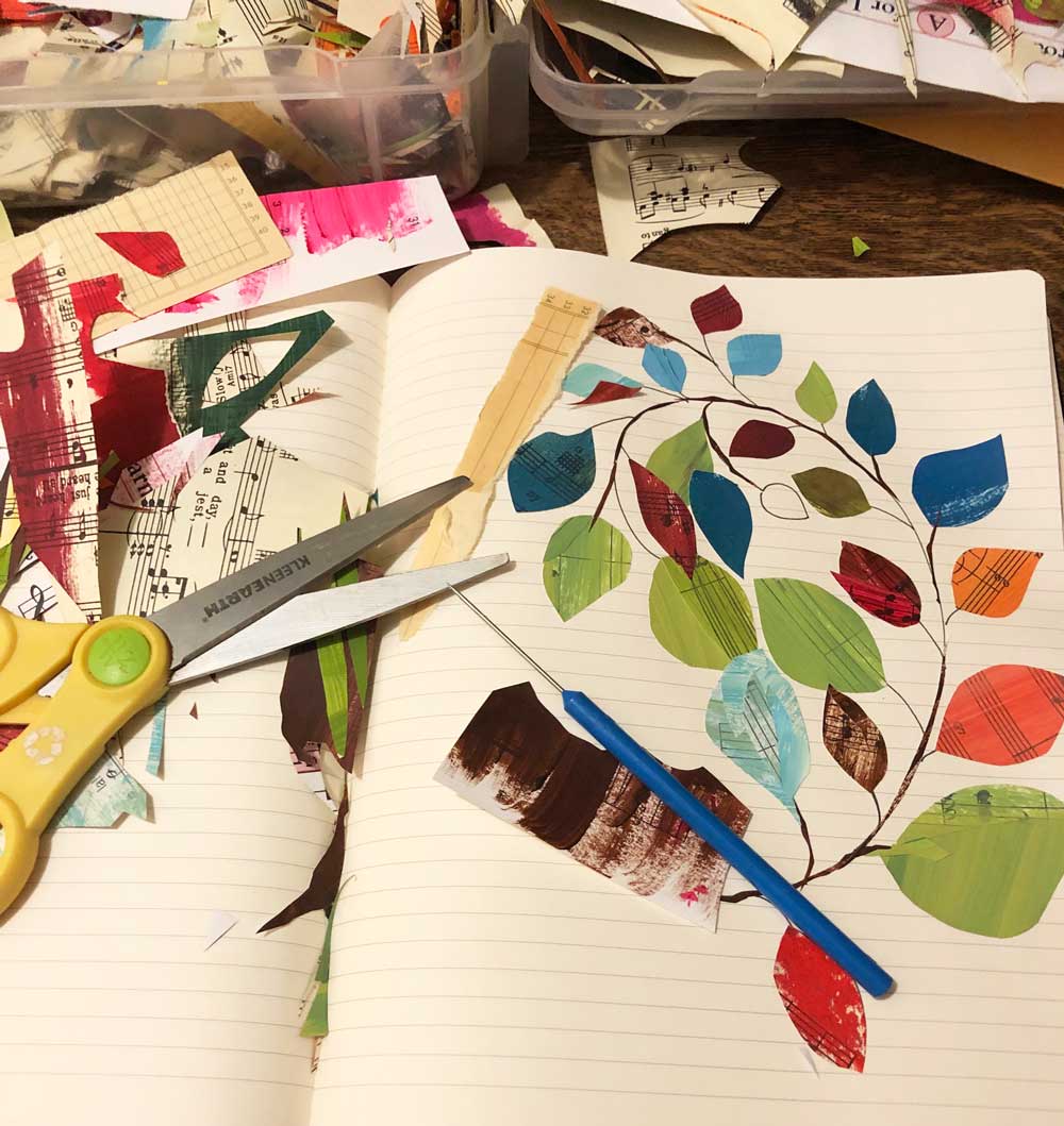 collage in progress - curled branch with colorful leaves on table with paper clippings and scissors