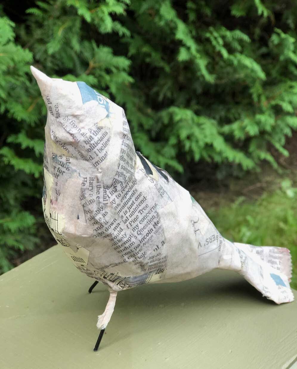 unfinished paper mache bird on post with pine tree background