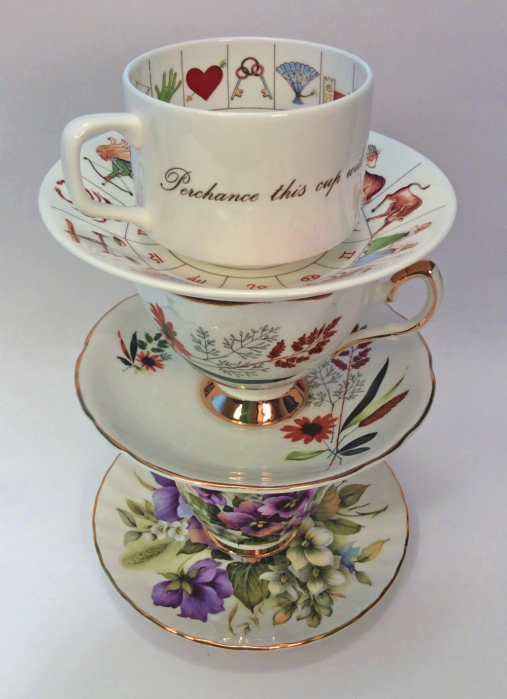 stack of three teacups with saucers: a tea-leave-reading set, autumn grasses, and violets